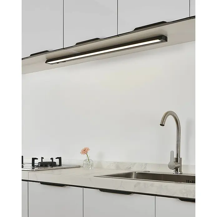 Eglo Lámpara LED bajo mueble Russcallo - L x An x Al: 87 x 2,4 x 6,1 cm, Negro - Tira de luz LED negra bajo armario, iluminando una encimera de cocina blanca con fregadero y vitrocerámica.