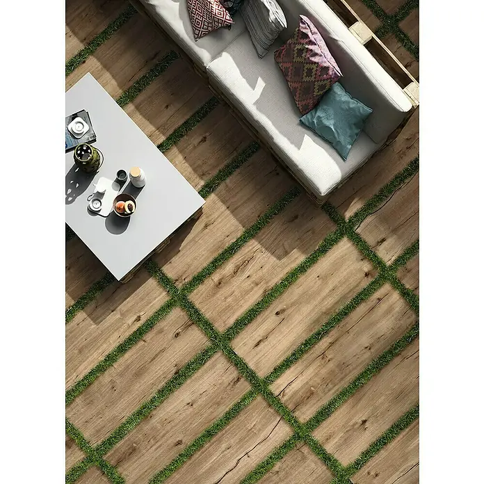 Terrassenfliese Essenze 2.0 - 40 x 120 x 2 cm, Honey, Matt - Outdoor-Terrasse mit Holzplankenboden, durchbrochen von grünen Grasstreifen, dazu ein helles Sofa und ein weißer Couchtisch.