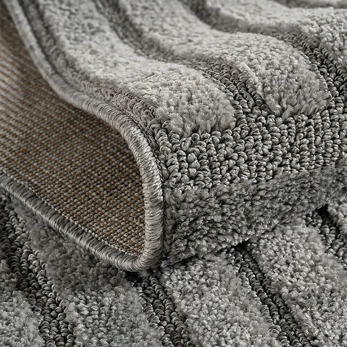 Kurzflorteppich Art 1123 - Silber, 200 x 140 cm, 100 % Polypropylen - Nahaufnahme eines grauen, strukturierten Teppichs mit Plüsch- und Schlingenflor, der seinen gekettelten Rand und die gewebte Unterseite zeigt.