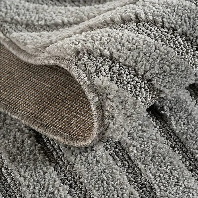 Kurzflorteppich Art 1122 - Silber, 170 x 120 cm, 100 % Polypropylen - Nahaufnahme eines grauen Teppichs mit abwechselnd flauschigen und geschlungenen Streifen. Der aufgerollte Rand zeigt die gewebte Rückseite.
