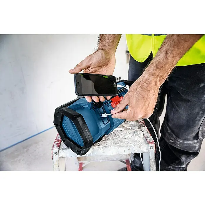 Bosch Professional AMPShare 18V Akku-Radio GPB 18V- 3 C SOLO K - 18 V, Ohne Akku - Ein Arbeiter lädt ein Smartphone mit einer blau-schwarzen tragbaren Powerstation/Arbeitsleuchte auf.