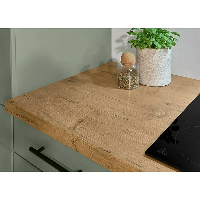 Respekta Küchenzeile Anton Typ 2 - Breite: 250 cm, Schilfgrün, Mit Elektrogeräten - Helle, holzfarbene Küchenarbeitsplatte mit integriertem Kochfeld, Gewürzglas und Pflanze.