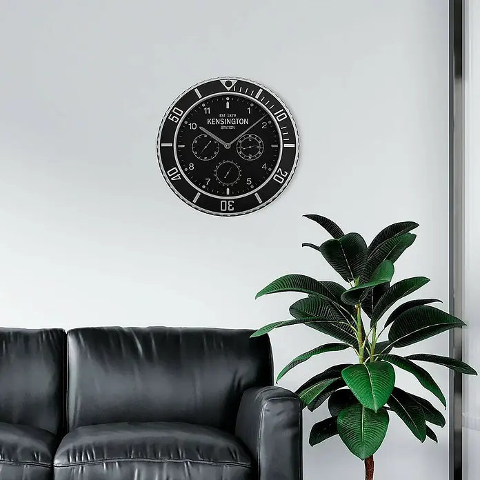 Versa Reloj de pared Bisel - Diámetro: 40 cm, Negro, Clásico - Gran reloj de pared negro y plateado estilo buceador con marca 'Kensington', colgado sobre un sofá negro.