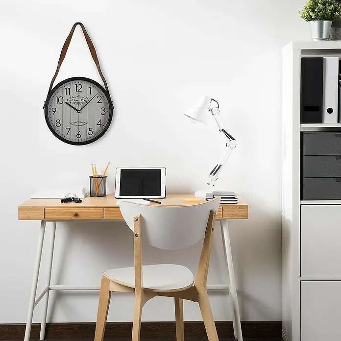 Versa Reloj de pared - Diámetro: 35 cm, Blanco/Negro, Clásico - Reloj de pared redondo negro con esfera blanca, números negros y correa de cuero marrón, colgado sobre un escritorio de madera.