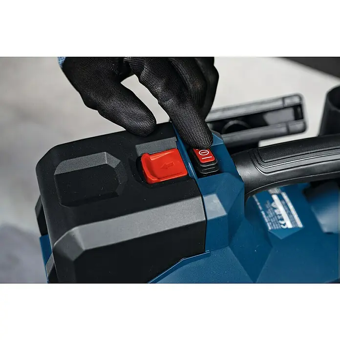 Bosch Professional AMPShare 18V Akku-Staubsauger GAS 18V-6 LS - 18 V, Behältervolumen: 4,5 l - Behandschuhte Hand drückt roten Einschaltknopf an blau-schwarzem Elektrowerkzeug. Ein roter Pfeilknopf ist ebenfalls sichtbar.