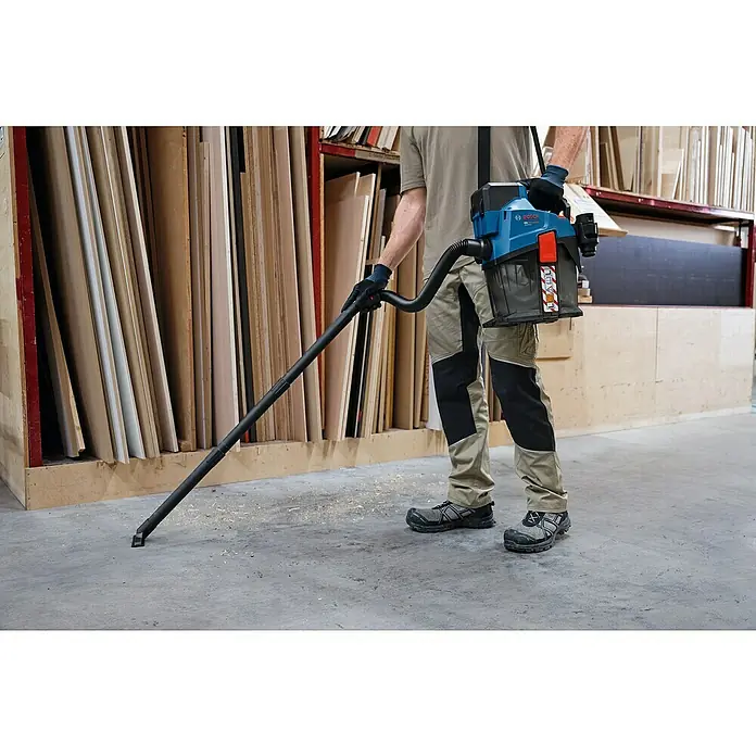 Bosch Professional AMPShare 18V Akku-Staubsauger GAS 18V-6 LS - 18 V, Behältervolumen: 4,5 l - Person reinigt mit blau-schwarzem Bosch Akku-Sauger Sägespäne auf Werkstattboden.