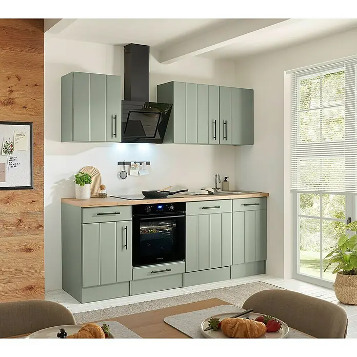Respekta Küchenzeile Anton Typ 2 - Breite: 220 cm, Schilfgrün, Mit Elektrogeräten - Moderne hellgrüne Küchenzeile mit Holz-Arbeitsplatte, integriertem Backofen und Spüle in einem hellen Raum.