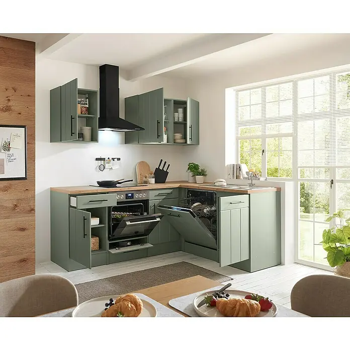 Respekta Winkelküche Anton Typ 1 - 172 x 220 cm, Schilfgrün, Mit Elektrogeräten - Moderne L-förmige Küche mit salbeigrünen Schränken, Holzoptik-Arbeitsplatte, integriertem Backofen und Geschirrspüler in hellem Raum mit großem Fenster.