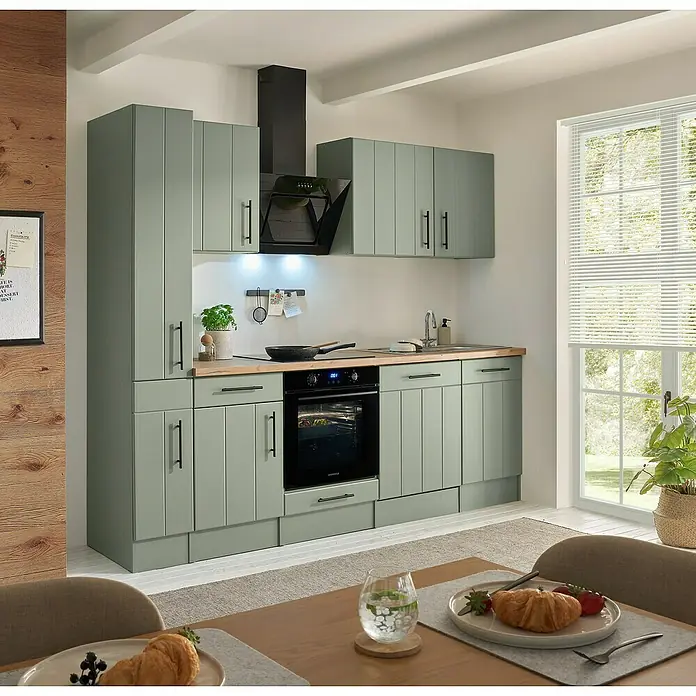 Respekta Küchenzeile Anton Typ 2 - Breite: 250 cm, Schilfgrün, Mit Elektrogeräten - Salbeigrüne Küchenzeile mit Holzplatte und schwarzen Geräten in heller Küche, komplett mit Backofen, Kochfeld, Spüle und Dunstabzugshaube.