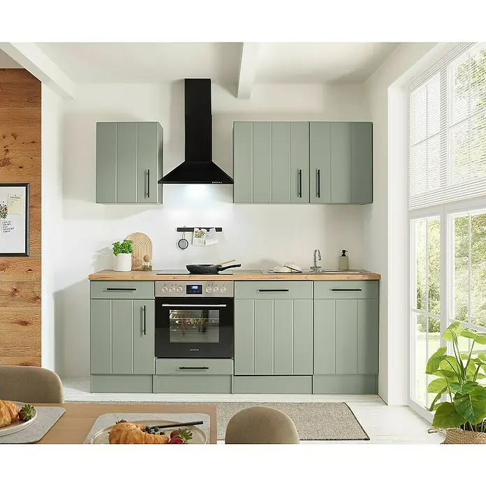 Respekta Küchenzeile Anton Typ 1 - Breite: 220 cm, Schilfgrün, Mit Elektrogeräten - Salbeigrüne Küchenzeile mit Holzplatte, integriertem Backofen, Kochfeld, Spüle und schwarzer Dunstabzugshaube in einer hellen Küche.