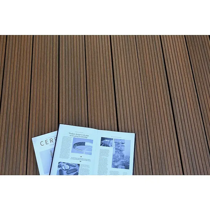 b!design WPC-Terrassendiele - 300 x 14,5 x 2,5 cm, Teak - Ein offenes Magazin über Produktdesign und Architektur liegt auf einem geriffelten Holzdeck.