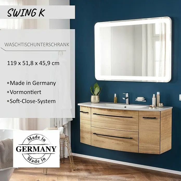 Camargue Swing K Waschtischunterschrank - 119 x 46 x 52 cm, Berg Eiche - Moderner Waschtischunterschrank aus hellem Holz mit weißem Waschbecken und schwarzen Griffen, darüber ein beleuchteter Spiegel an dunkelblauer Wand.