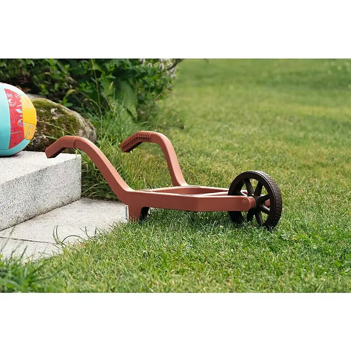 Lechuza Dekofigur Schubkarre - L x B x H: 68 x 30 x 20 cm, Kunststoff - Braune Plastik-Spielzeugschubkarre, neben einem bunten Wasserball und einer Steinstufe.