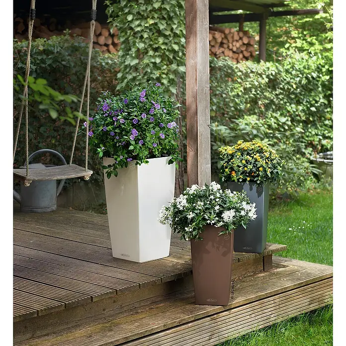 Lechuza Color Pflanzsäule eckig Cubico - Außenmaß (L x B x H): 22 x 22 x 41 cm, Kunststoff, Muskat - Drei hohe, rechteckige Pflanzgefäße in Weiß, Braun und Dunkelgrau, bepflanzt mit blühenden Pflanzen, auf einer Holzterrasse.
