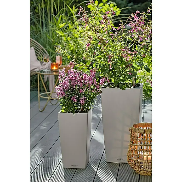 Lechuza Color Pflanzsäule eckig Cubico - Außenmaß (L x B x H): 30 x 30 x 56 cm, Kunststoff, Sandbraun - Zwei hohe, hellgraue rechteckige Pflanzgefäße mit leuchtend rosa Blütenpflanzen auf einer Außenterrasse.