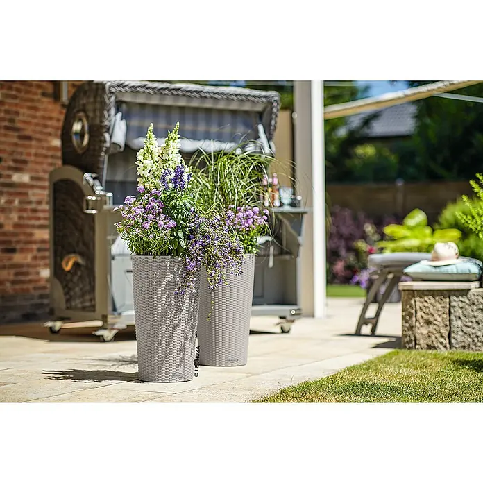Lechuza Cottage Pflanzsäule rund Cilindro - Außenmaß (Ø x H): 23 x 41 cm, Kunststoff, Sandbraun - Zwei hellgraue Pflanzgefäße von Lechuza in Korboptik, gefüllt mit bunten Blumen und Pflanzen auf einer Terrasse.