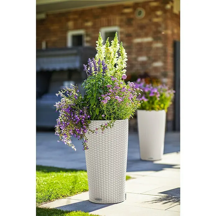 Lechuza Cottage Pflanzsäule rund Cilindro - Außenmaß (Ø x H): 23 x 41 cm, Kunststoff, Grau - Hoher weißer geflochtener Pflanzkübel mit lila und gelben Blumen auf einer sonnigen Terrasse.
