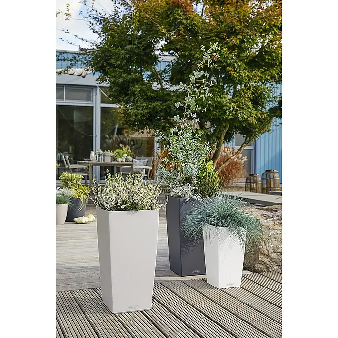 Lechuza Cottage Pflanzsäule eckig Cubico 40 - Außenmaß (L x B x H): 39,5 x 39,5 x 75,5 cm, Kunststoff, Lichtgrau - Drei hohe, eckige Pflanzgefäße in Weiß, Hellgrau und Anthrazit, bepflanzt mit verschiedenen Pflanzen, auf einem Holzdeck als Teil eines Outdoor-Wohnbereichs.
