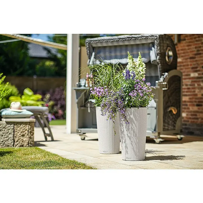 Lechuza Cottage Pflanzsäule rund Cilindro - Außenmaß (Ø x H): 32 x 56 cm, Kunststoff, Lichtgrau - Zwei weiße Pflanzgefäße mit Korbgeflecht-Optik, gefüllt mit lila und weißen Blumen, auf einer sonnigen Terrasse.