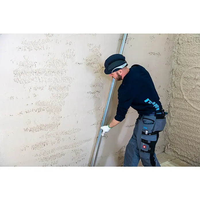 Knauf Maschinenputz MP 75 L - 30 kg, Innen - Arbeiter glättet mit einer Richtlatte frisch aufgetragenen Putz an einer Wand.