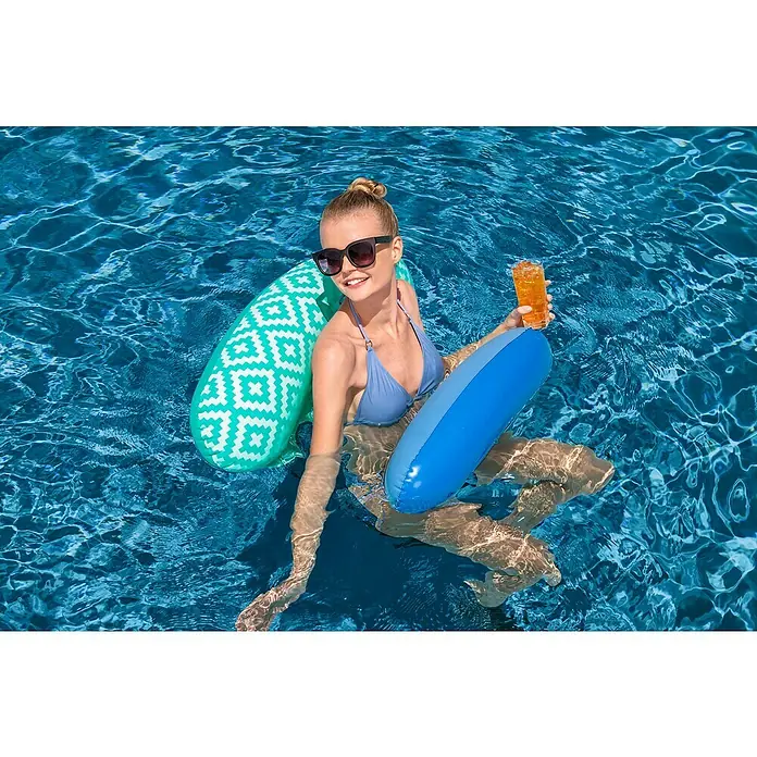 Bestway Luftmatratze Comfort Plus Pool-Hängematte - L x B: 80 x 124 cm - Frau entspannt in blauem Pool, gestützt von grün-weiß gemusterter Luftmatratze und blauem Schwimmkissen, mit Getränk.