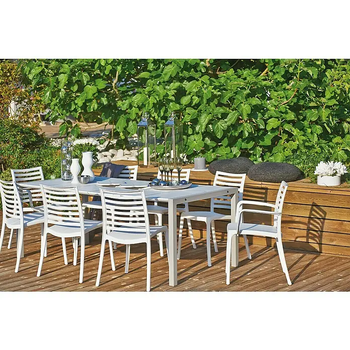 Grosfillex Stapelsessel Set Sunday - 4 Stk., Polypropylen, Stapelbar, Weiß, B x T x H: 59 x 56 x 84 cm - Weißes Garten-Esstisch- und Stuhlset auf einer Holzterrasse, bereit für eine Mahlzeit inmitten grüner Pflanzen.