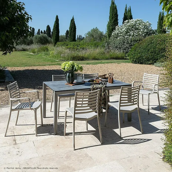 Grosfillex Stapelsessel Set Sunday - 4 Stk., Polypropylen, Stapelbar, Beige, B x T x H: 59 x 56 x 84 cm - Hellgraues Outdoor-Essset mit rechteckigem Tisch und sechs Lamellenstühlen auf einer Terrasse arrangiert.