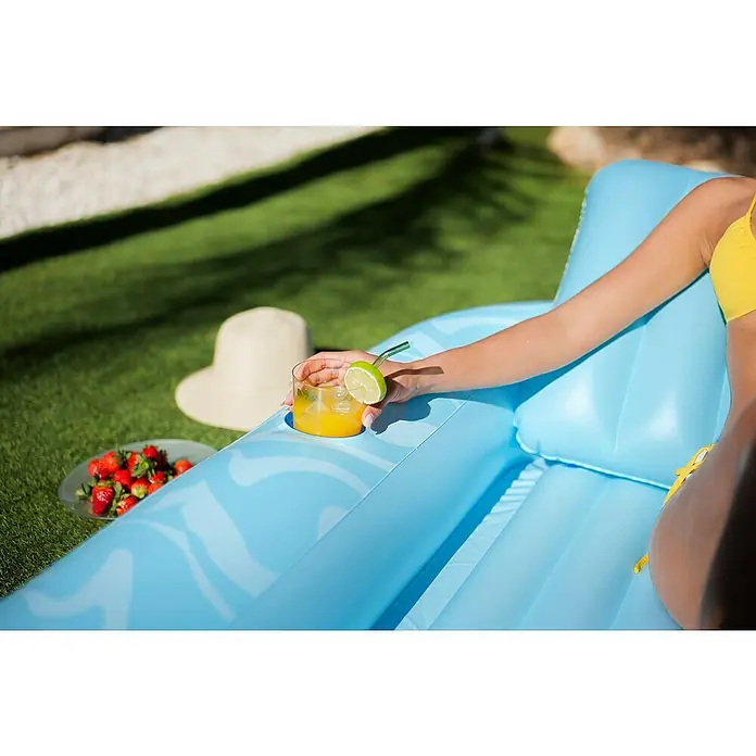 Bestway Luftmatratze Tanning Lounge - L x B: 1,37 x 2,03 m - Eine Person entspannt auf einer hellblauen aufblasbaren Poolliege mit Getränkehalter und hält ein Getränk.
