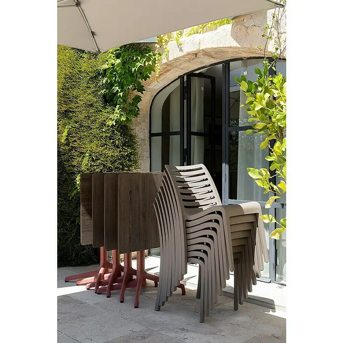 Grosfillex Stapelstuhl Set Slat - 4 Stk., Polypropylen, Stapelbar, Taupe, B x T x H: 53 x 58 x 88 cm - Gestapelte taupefarbene Plastikstühle und zusammengeklappte Tische mit braunen Platten und rötlichen Gestellen auf einer Terrasse.