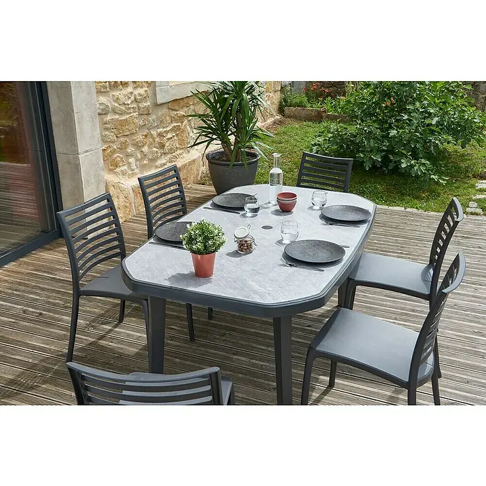 Grosfillex Stapelstuhl Set Sunday - 4 Stk., Polypropylen, Stapelbar, Anthrazit, B x T x H: 50 x 56 x 84 cm - Graues Outdoor-Essset mit ovalem Tisch und sechs Stühlen auf einer Holzterrasse. Für eine Mahlzeit gedeckt.