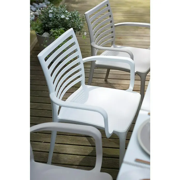 Grosfillex Stapelstuhl Set Sunday - 4 Stk., Polypropylen, Stapelbar, Weiß, B x T x H: 50 x 56 x 84 cm - Zwei weiße und hellgraue Kunststoff-Gartenstühle mit Lamellenlehnen auf einer Holzterrasse, die einen Essbereich im Freien andeuten.