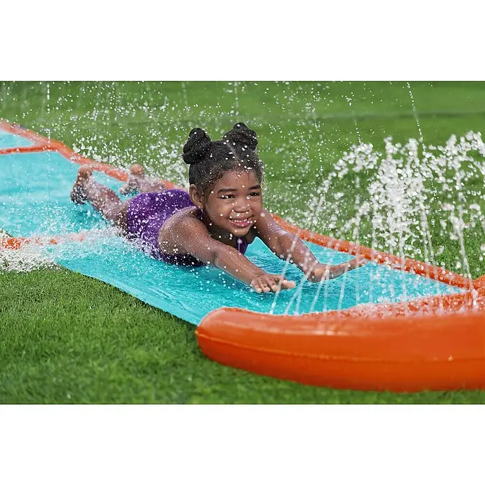 Bestway Wasserrutsche H2OGO! Fontäne - Aquamarin/Orange - Ein lächelndes Kind rutscht auf einer blauen Wasserrutsche mit orangefarbenen aufblasbaren Seiten, umgeben von Wassersprühstrahlen.