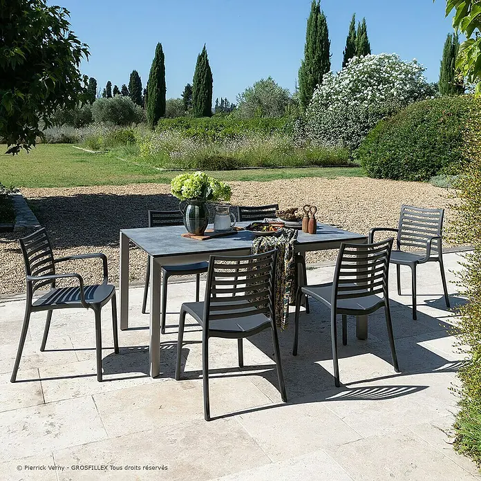 Grosfillex Gartentisch Greggia - L x B x H: 160 x 95 x 74,5 cm, Aluminium, HPL, Grau - Graue Outdoor-Essgruppe (Tisch und Stühle) auf einer Terrasse in einem sonnigen Garten.