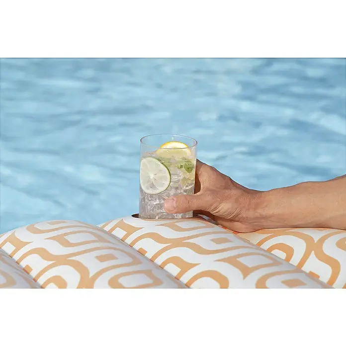 Bestway Luftmatratze mit Samtoberfläche - L x B: 77,5 x 169 cm - Hand hält Getränk in Becherhalter auf aufblasbarer Poolliege mit weiß-orangefarbenem geometrischem Muster im Schwimmbad.