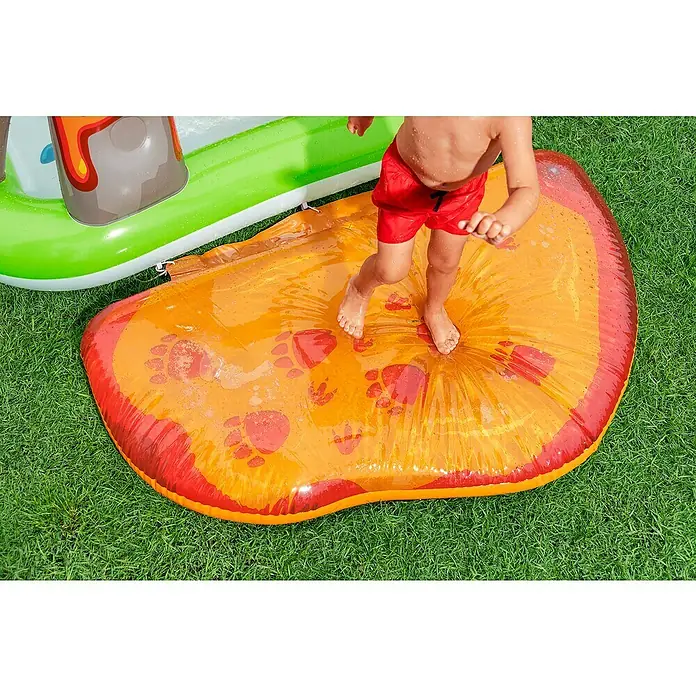 Bestway Planschbecken Wasserspielcenter Vulkan - 188 x 262 x 102 cm - Kind spielt auf gelb-roter aufblasbarer Wasserspielmatte mit Dino-Abdrücken, nahe grünem Planschbecken.