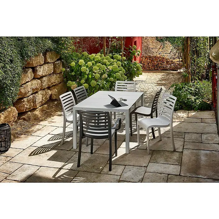 Grosfillex Stapelstuhl Set Slat - 4 Stk., Polypropylen, Stapelbar, Anthrazit, B x T x H: 53 x 58 x 88 cm - Hellgrauer Gartentisch mit hell- und dunkelgrauen Stühlen auf einer Steinterrasse.