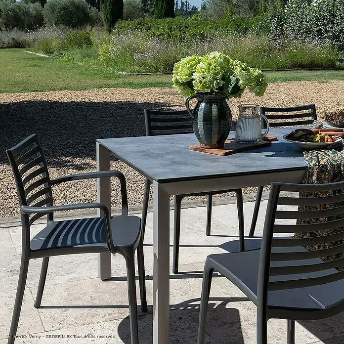 Grosfillex Stapelsessel Set Sunday - 4 Stk., Polypropylen, Stapelbar, Anthrazit, B x T x H: 59 x 56 x 84 cm - Anthrazitfarbene Outdoor-Tisch- und Stuhlgarnitur mit Armlehnen und Lattenrücken auf einer Terrasse.