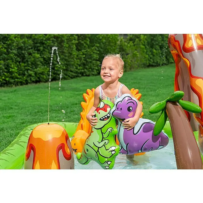 Bestway Planschbecken Wasserspielcenter Vulkan - 188 x 262 x 102 cm - Kind spielt fröhlich in einem farbenfrohen aufblasbaren Dino-Planschbecken mit Wassersprinklern.