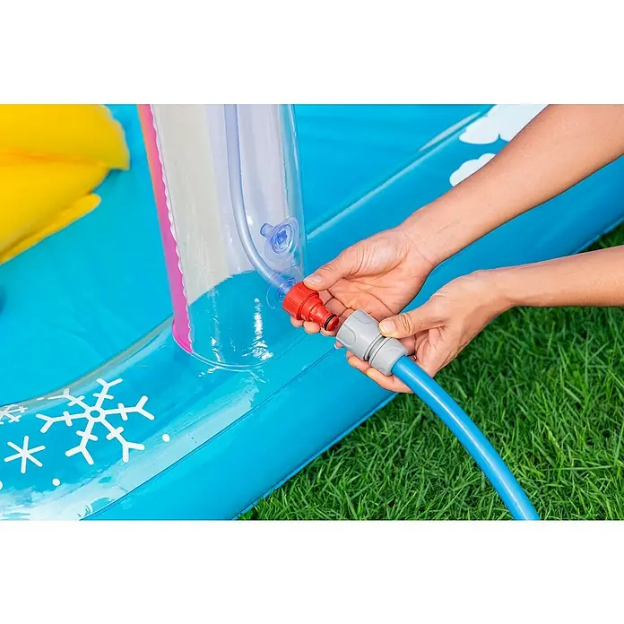 Bestway Planschbecken Wasserspielcenter Regenbogen - 150 x 188 x 89 cm - Hände verbinden einen blauen Gartenschlauch mit einem grauen Adapter an ein rotes Ventil eines transparenten Teils eines blauen aufblasbaren Wasserspielplatzes.