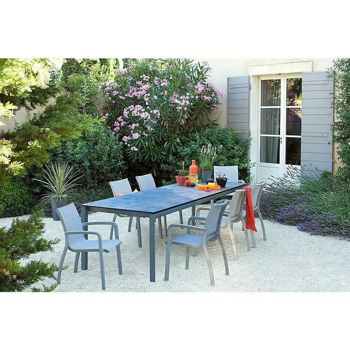 Grosfillex Gartentisch Greggia - L x B x H: 220 x 95 x 74,5 cm, Aluminium, HPL, Grau - Eine Outdoor-Essgruppe mit einem dunkelgrauen rechteckigen Tisch und acht grauen Stühlen, umgeben von Gartengrün.