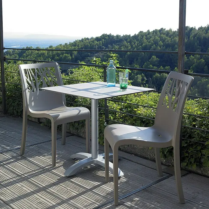 Grosfillex Stapelstuhl Set Vegetal - 4 Stk., Polypropylen, Taupe, B x T x H: 60 x 58 x 88 cm - Zwei graue Stühle mit baumförmigen Rückenlehnen und ein passender quadratischer Tisch auf einer Holzterrasse mit Talblick.