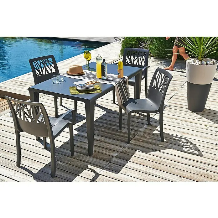Grosfillex Stapelsessel Set Vegetal - 4 Stk., Polypropylen, Anthrazit, B x T x H: 60 x 58 x 88 cm - Dunkelgraues Outdoor-Esstischset aus Kunststoff mit Tisch und vier Stühlen mit Astmuster-Rückenlehnen auf einer Holzterrasse am Pool.