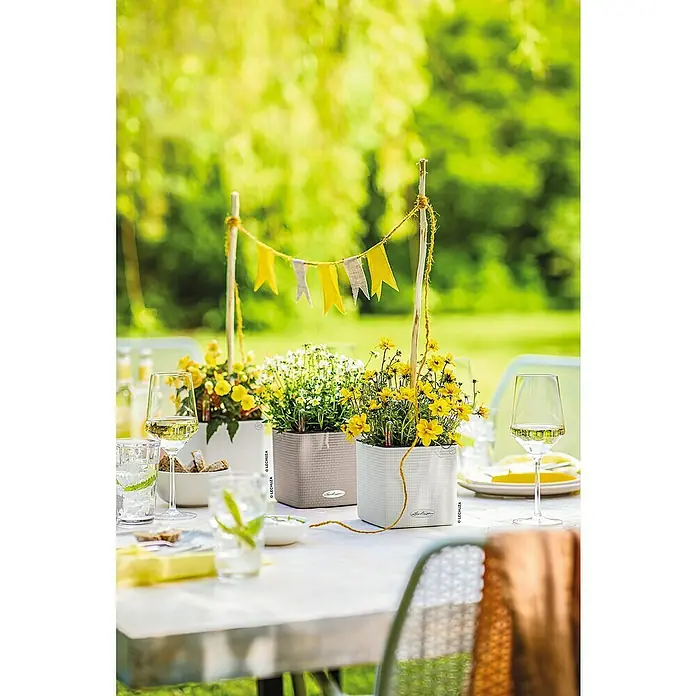 Lechuza Classico Kräutertopf Color - Außenmaß (L x B x H): 14 x 14 x 14 cm, Kunststoff, Sandbraun - Weiße und taupefarbene, selbstbewässernde Würfel-Pflanzgefäße mit strukturierter Oberfläche, bepflanzt mit Blumen auf einem Gartentisch.