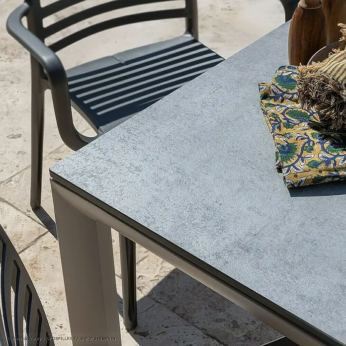 Grosfillex Gartentisch Greggia - L x B x H: 220 x 95 x 74,5 cm, Aluminium, HPL, Grau - Esstisch für den Außenbereich mit grauer, strukturierter Platte und dunkelgrauem Stuhl auf einer Terrasse.