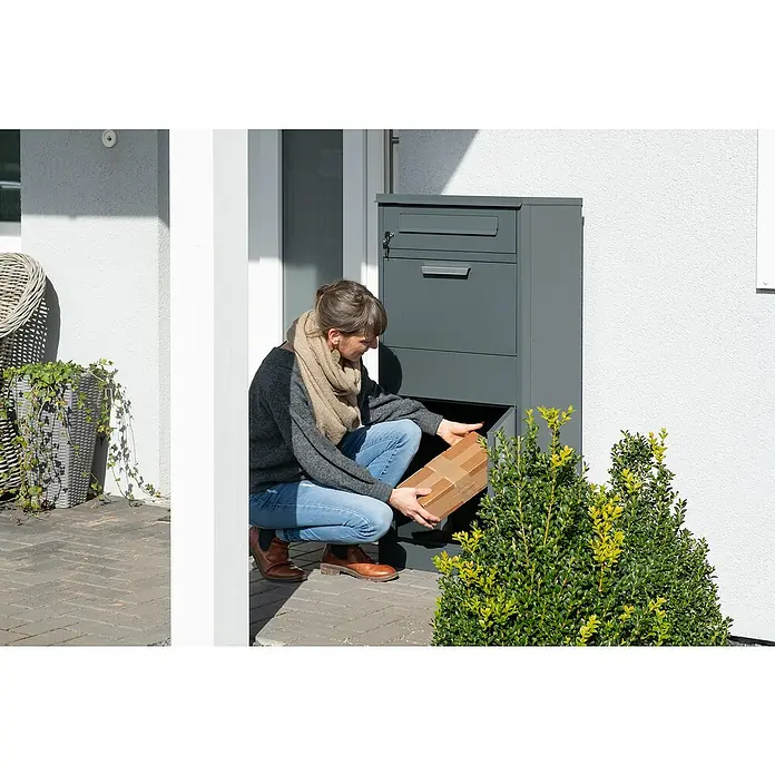 Westmann Paketbox Pedro - Höhe: 112 cm, Grau, Stahl - Eine Person legt ein Paket in eine dunkelgraue Paketbox aus Metall am Hauseingang.