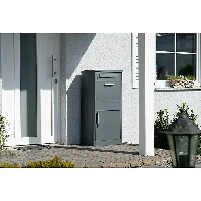 Westmann Paketbox Pedro - Höhe: 112 cm, Grau, Stahl - Ein moderner grauer Paketbriefkasten steht neben einer weißen Haustür, bereit für Post und Pakete.