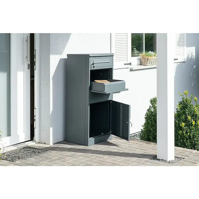 Westmann Paketbox Pedro - Höhe: 112 cm, Grau, Stahl - Ein grauer Paketbriefkasten aus Metall steht neben einem Hauseingang, das Paketfach ist geöffnet mit einem kleinen Paket darin.