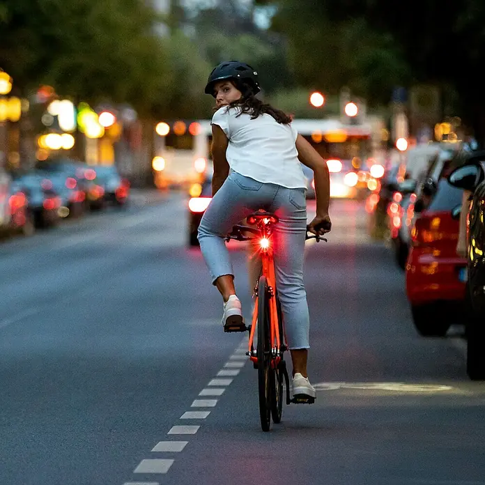 Sigma Fahrradbeleuchtungs-Set Aura 30/Curve - 2 -tlg., Mit Batterien - Ein Radfahrer mit Helm fährt nachts auf einem Stadtrad mit hellrotem Rücklicht auf einer Straße.