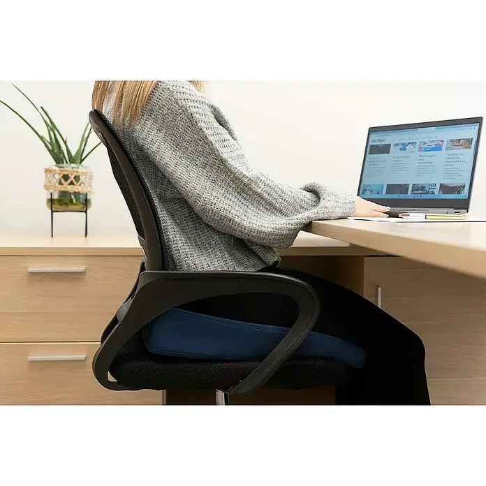Cojín para respaldo - Azul marino, Relleno de espuma - Una persona usa un cojín de asiento ergonómico azul en una silla de oficina mientras trabaja en un escritorio.