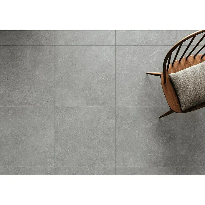 DryTile Feinsteinzeugfliese Silkstone Schlamm - 60 x 60 cm, Grau, Matt - Graue Steinoptik-Bodenfliesen, von oben gesehen, mit Holzstuhl und Kissen.